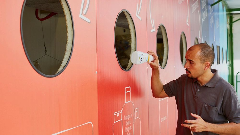 Man deposits a plastic bottle into a large colorful recycling station wall.